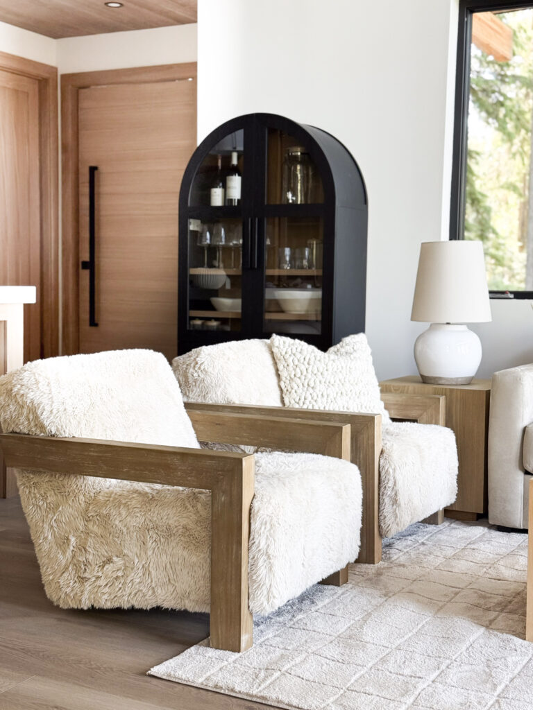 cabin decor essentials | a photo featuring fur accent chairs, a rounded arch cabinet in the background, a neutral area rug