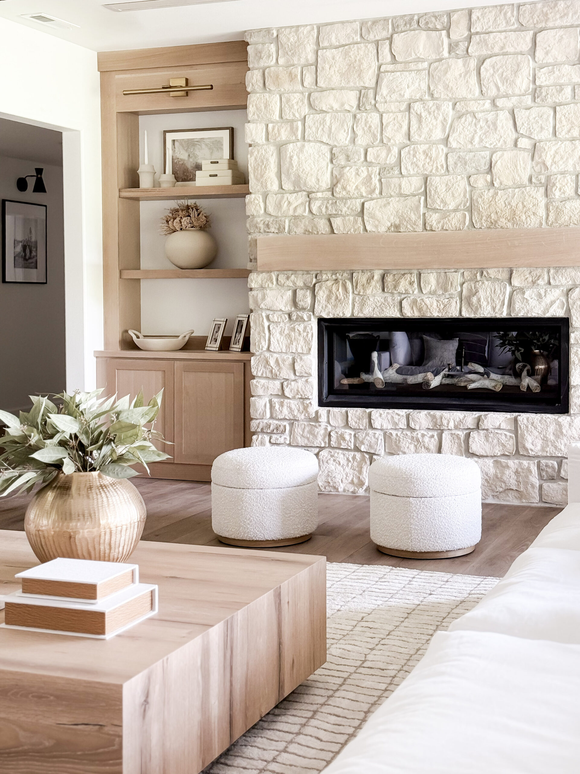 organic modern basement reveal featuring a fireplace and stone wall, custom built-ins, coffee table, ottomans, faux greenery