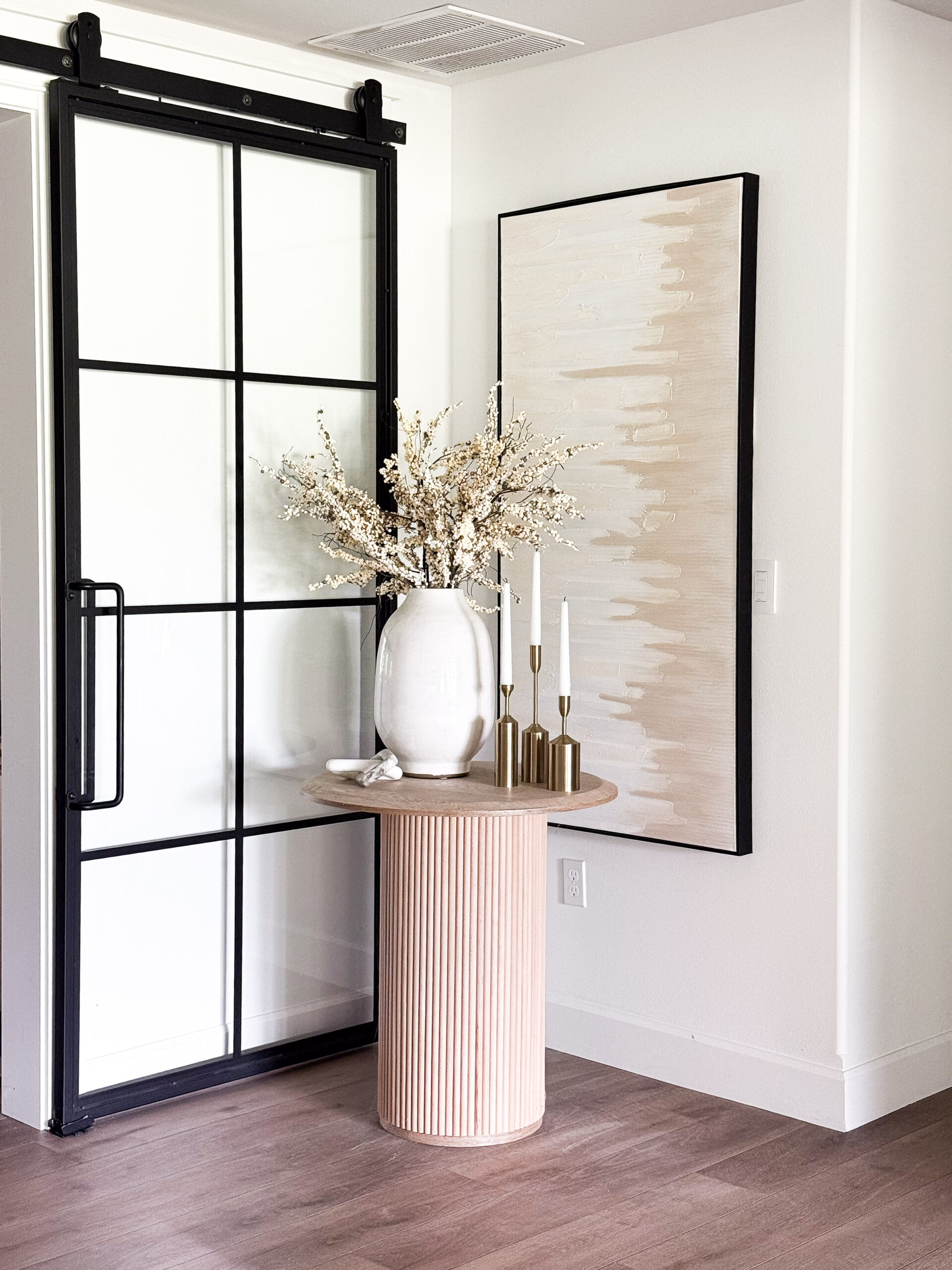 organic modern basement reveal featuring accent table, faux florals, candles, wall art, marble decor