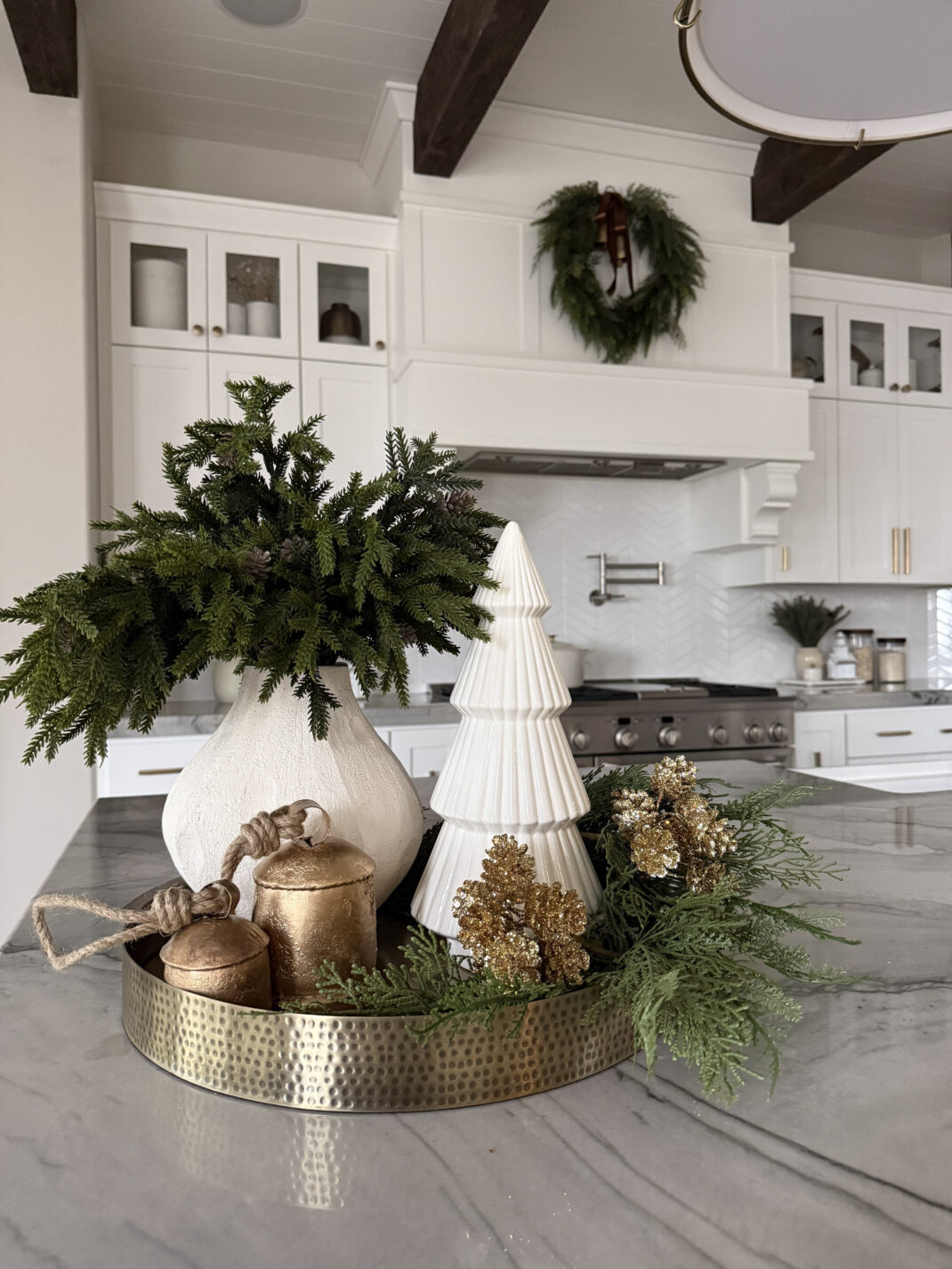 Kitchen counter decorated with gold bells, a small ceramic Christmas tree, and holiday greenery.