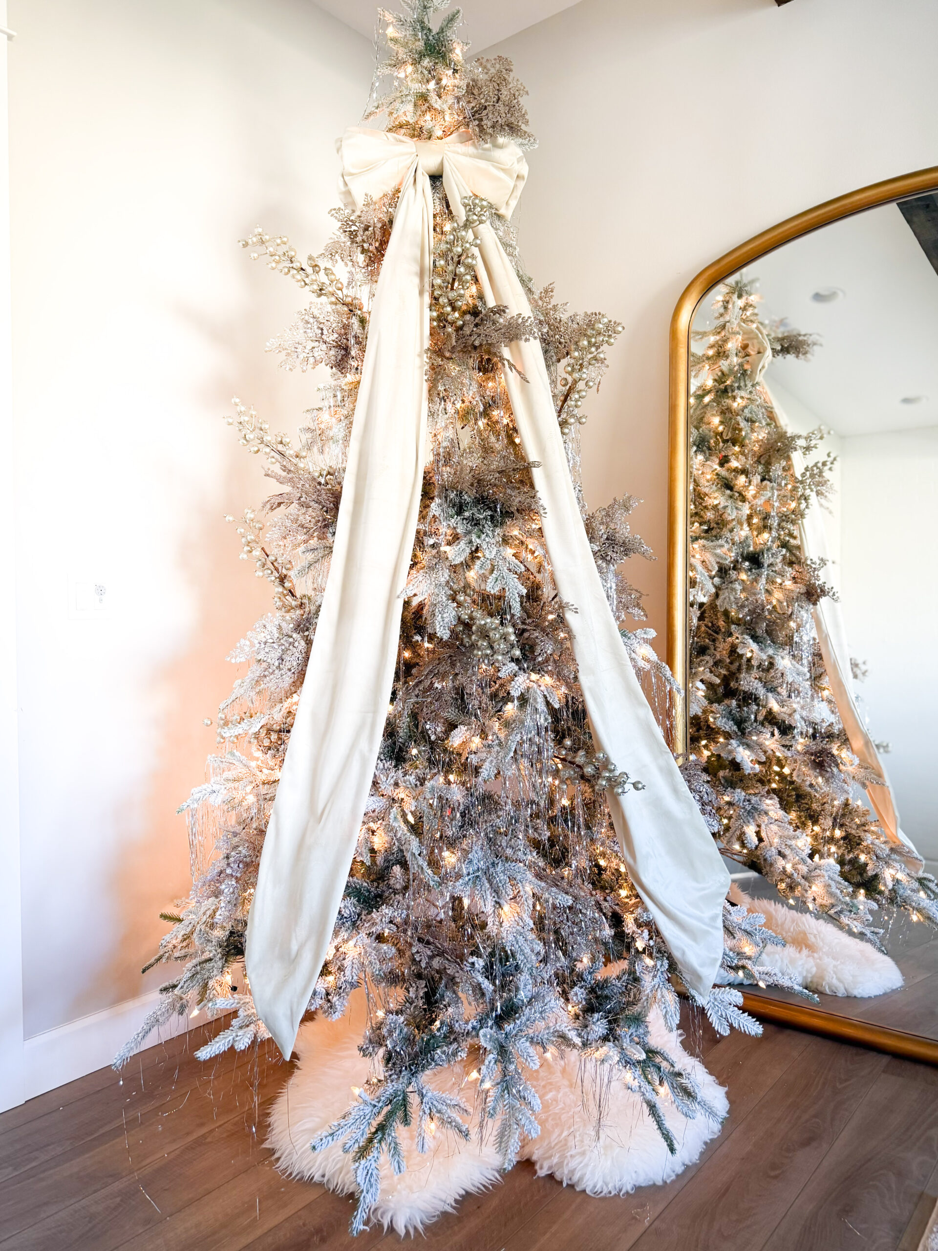 Flocked Christmas tree with a large festive bow as a topper, styled for a cozy holiday feel.